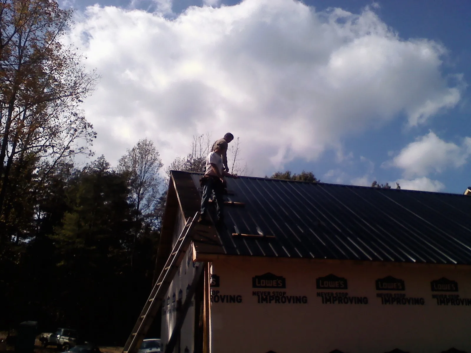 Roofer fastening dark metal panels high against a cloudy sky, from a Roof Inspection job in Hanover